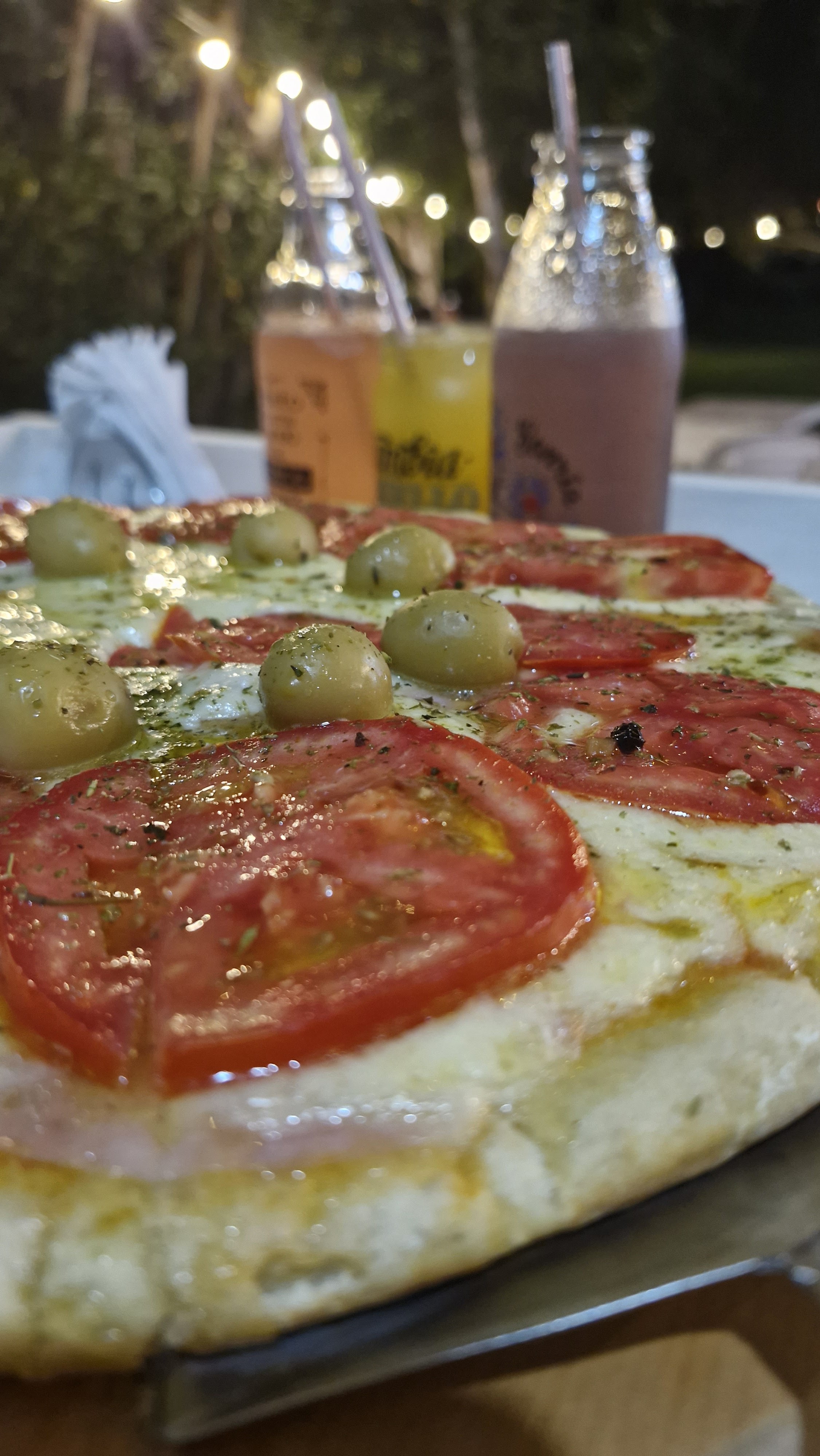 Pizza napolitana con aceitunas y de fondo licuados y jugos